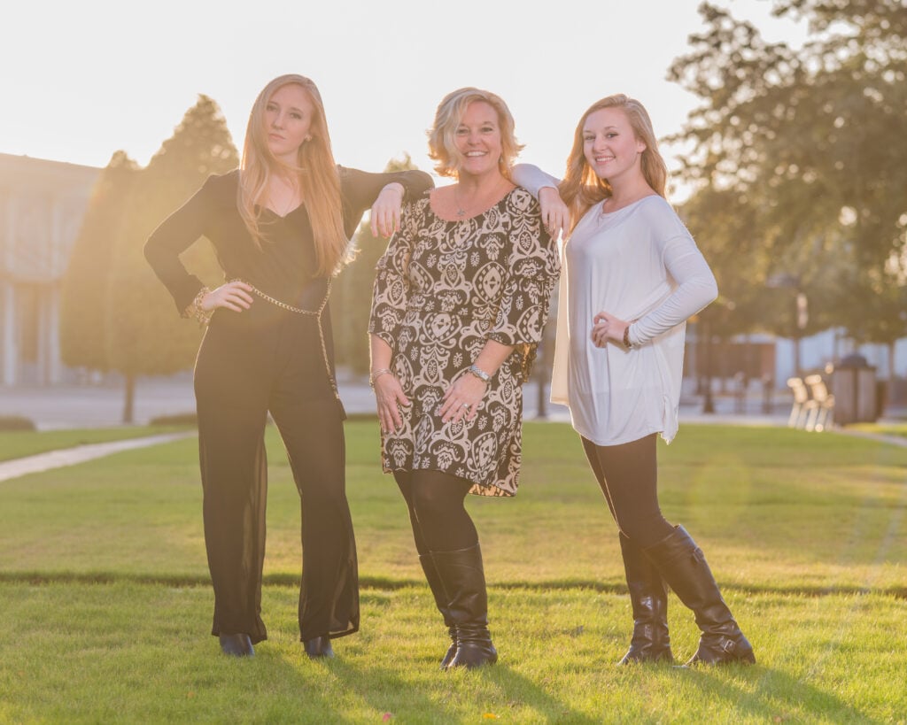 Three women posing outdoors in sunlight.